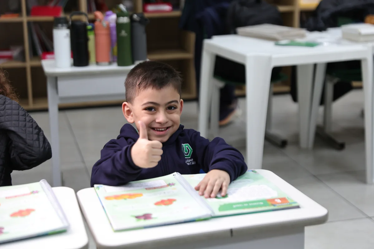 Aluno do Colégio Universitário sorrindo e fazendo sinal de positivo em sala de aula