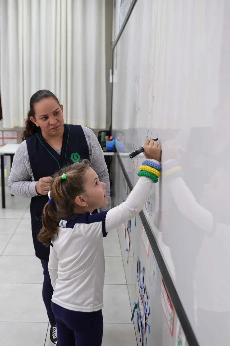 Aluna do Colégio Universitário escrevendo no quadro com o apoio de uma professora